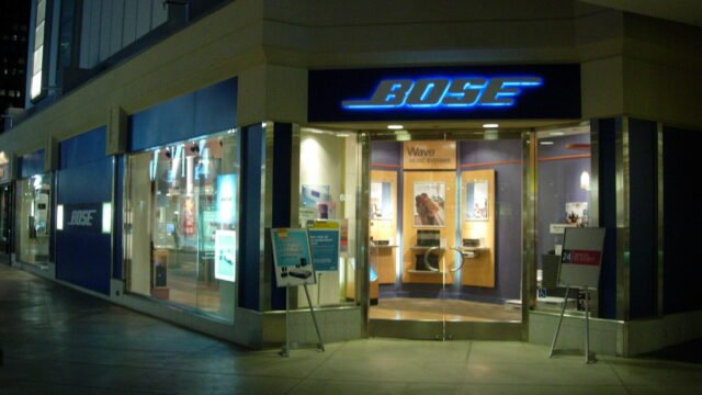 Вход на фирмен магазин на Bose със светещо синьо лого над вратата и витрини със системи Wave
