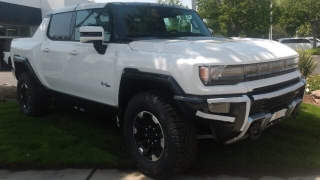 Бял електрически пикап GMC Hummer EV, сериен модел от 2022 г., паркиран на тревна площ, изглед отпред и отстрани