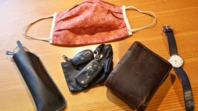 Платнена маска на дървена маса до очила в кожен калъф, ключове, портфейл и часовник