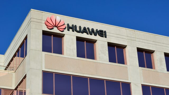 Фасада на офис сграда с червеното лого и надписа HUAWEI на фона на синьо небе