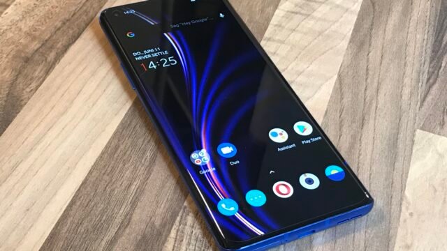 Син смартфон OnePlus 8 Pro с включен екран върху дървена маса