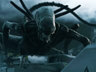 Ксеноморфът от поредицата Alien пълзи по метална конструкция на фона на облачно небе