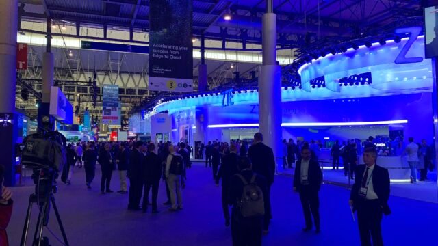 Посетители в изложбена зала на Mobile World Congress в Барселона, осветена в синьо