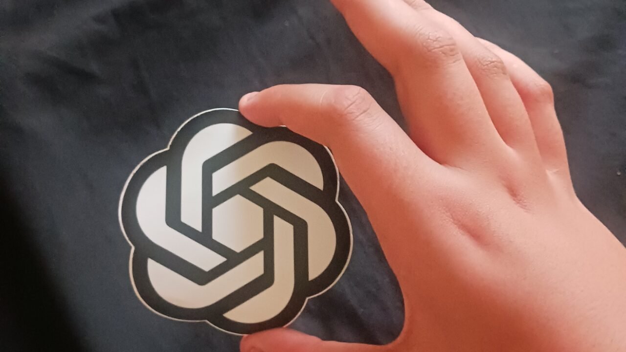 Ръка държи стикер с логото на OpenAI, компанията зад ChatGPT for Teens