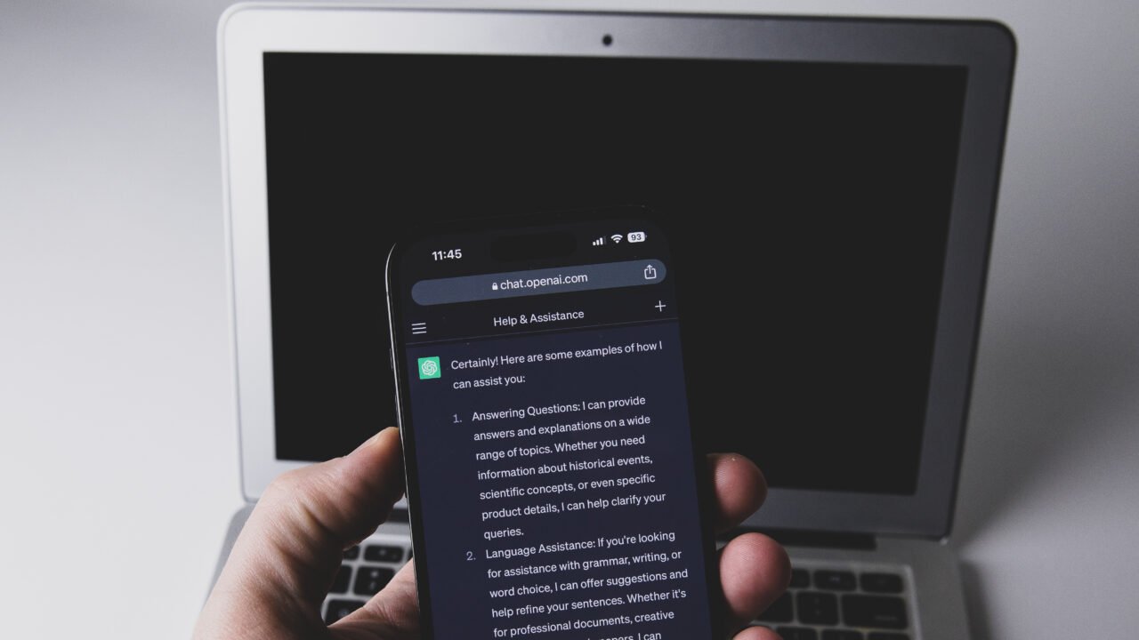 Смартфон с чат в ChatGPT пред лаптоп – заключени чатове в ChatGPT