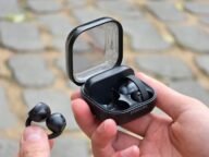Отворените слушалки Galaxy Buds On с клипс и кутията им за зареждане в ръка