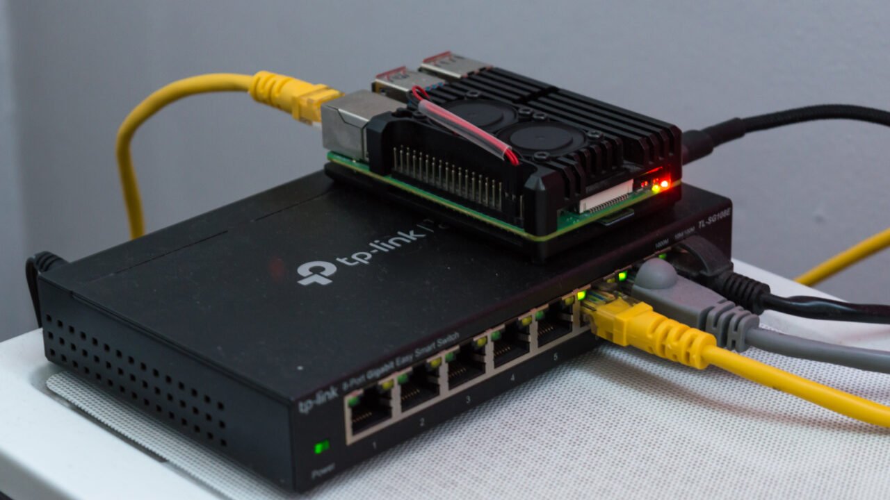 Raspberry Pi 4 в метален корпус върху мрежов суич – типичен сървър за Home Assistant, чиито резервни копия трябва да пазите