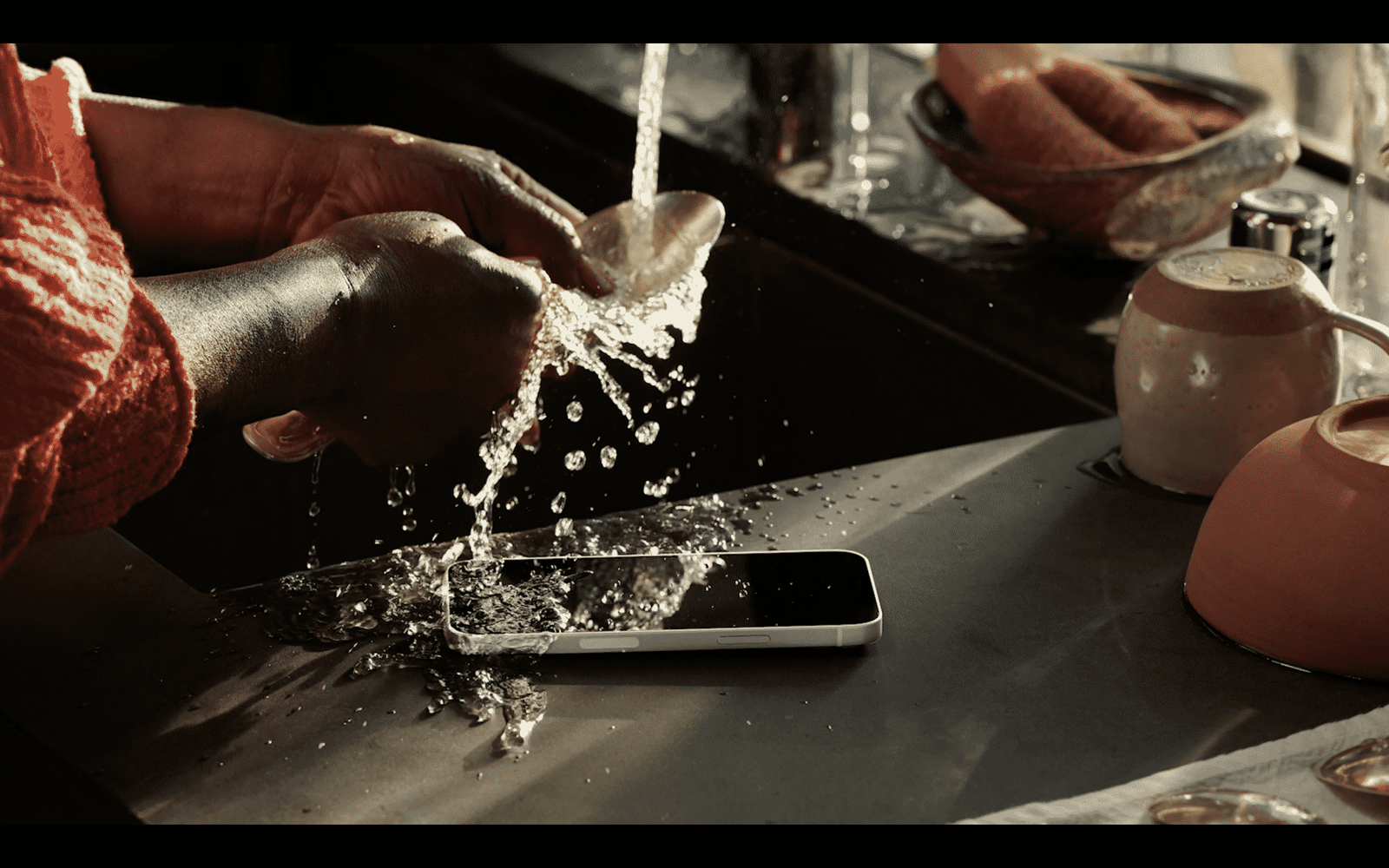 iPhone 13 върху мокър плот под течаща вода – демонстрация на водоустойчивостта