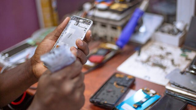 Ръце държат разглобен корпус на смартфон на ремонтен плот – илюстрация за официалните ръководства за ремонт на iPhone Duo
