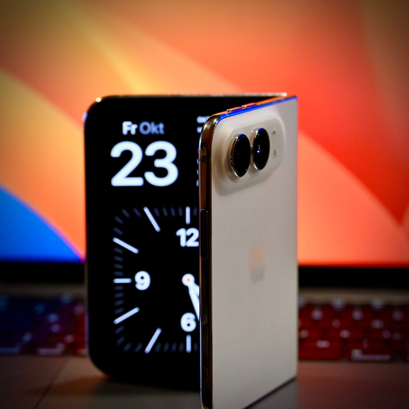 Полуотворен iPhone Duo пред лаптоп – външният екран показва часовник