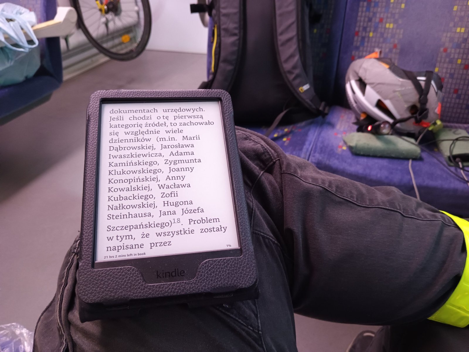 Електронен четец Kindle Paperwhite в черен калъф с отворена книга на полски, държан в купе на влак