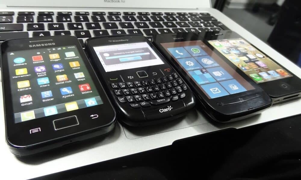 Четири по-стари смартфона с Android, BlackBerry, Windows Phone и iOS, подредени върху клавиатура на лаптоп