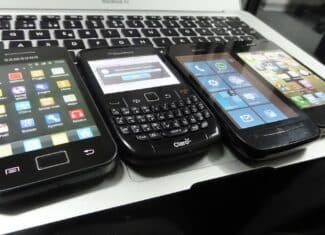 Четири по-стари смартфона с Android, BlackBerry, Windows Phone и iOS, подредени върху клавиатура на лаптоп