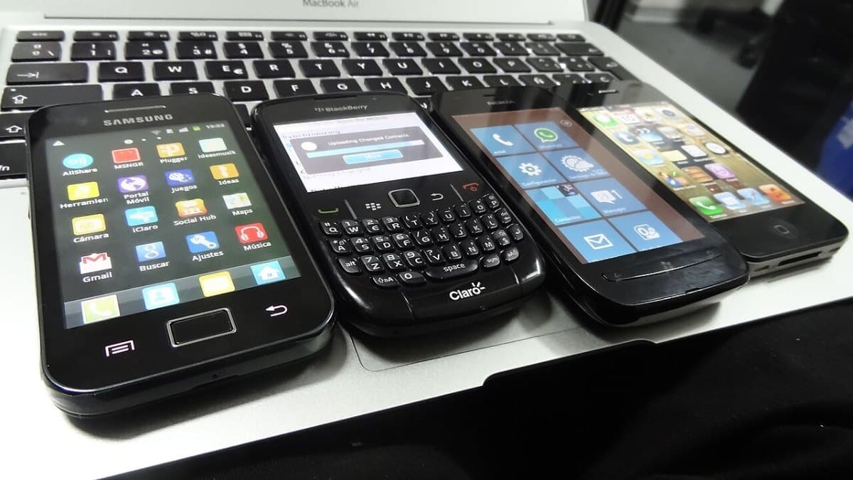 Четири по-стари смартфона с Android, BlackBerry, Windows Phone и iOS, подредени върху клавиатура на лаптоп